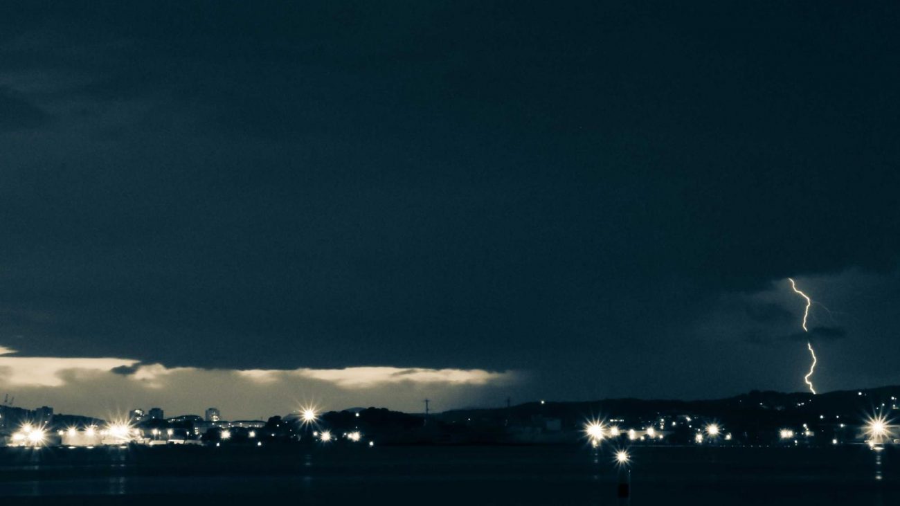 A neat stack of contemporary indie press novels with subtle minimalist covers placed on a worn wooden writing desk beside a small ceramic cup of espresso and a fountain pen.