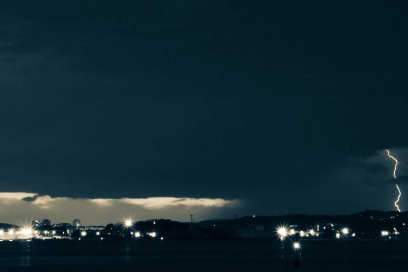 A neat stack of contemporary indie press novels with subtle minimalist covers placed on a worn wooden writing desk beside a small ceramic cup of espresso and a fountain pen.