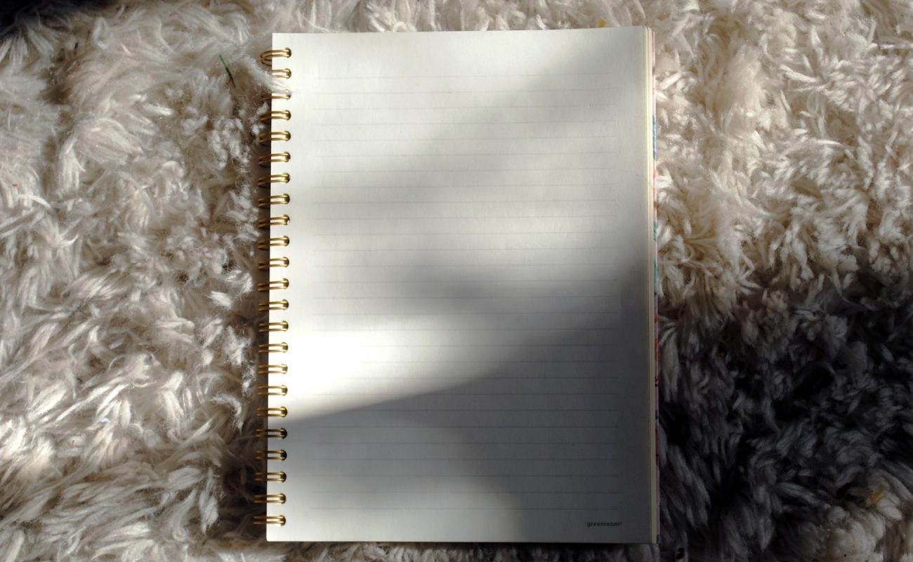 A small stack of contemporary essay collections beside a half-empty cup of coffee on a bright wooden table, with a paperback by Annie Ernaux on top, sunlight falling diagonally across the page edges.