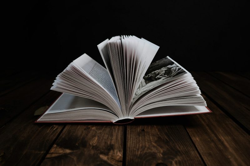 An open bilingual poetry edition on a dark wooden table showing the original Spanish text on the left page and the English translation on the right, with annotations in pencil and a small lamp casting warm light.