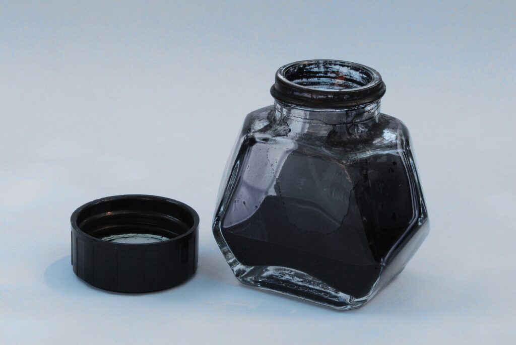 Encrier en verre et porte-plume pos&eacute;s pr&egrave;s d'une feuille couverte de vers