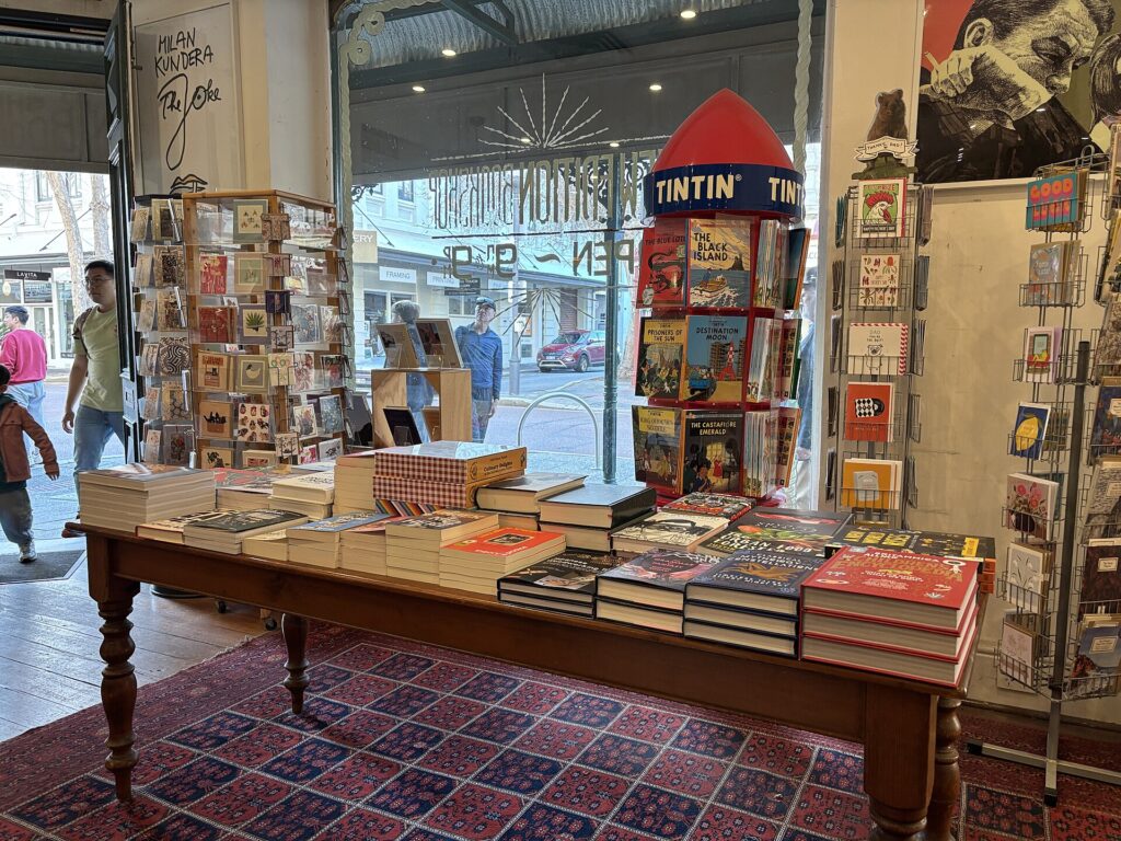 Table de librairie couverte de piles de romans récents, couvertures claires et bandeaux imprimés