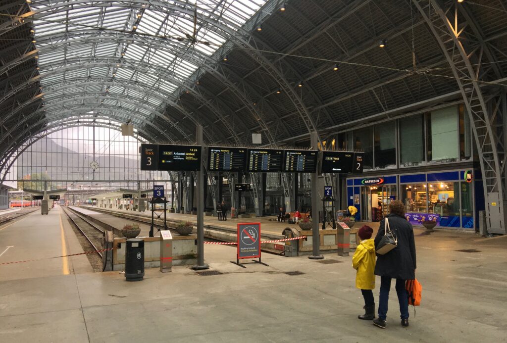 Grand hall de gare avec tableau des départs, quelques personnes assises sur des bancs
