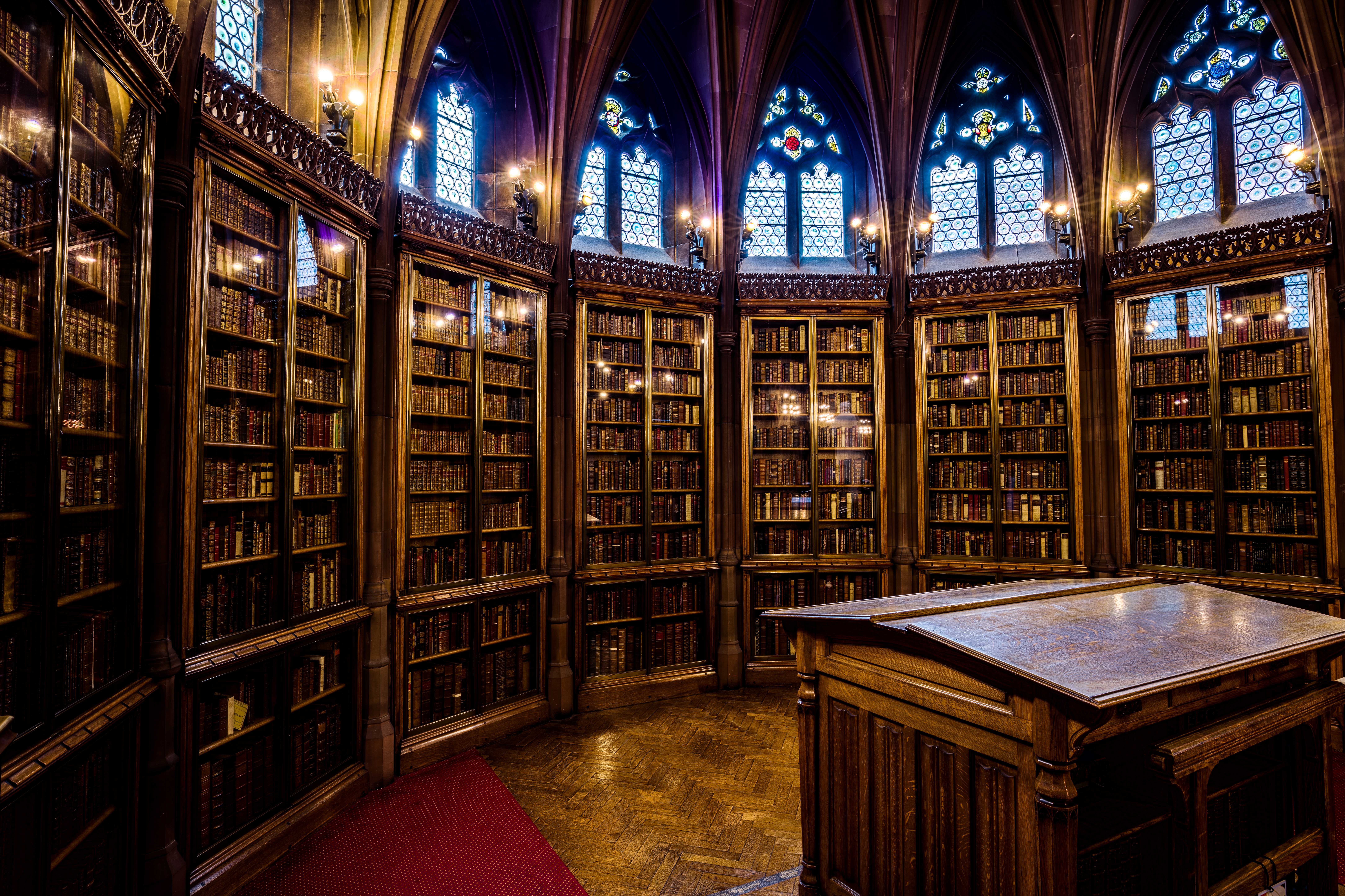 Table de lecture en bois dans une salle de bibliothèque, lampe basse et rayonnages au fond