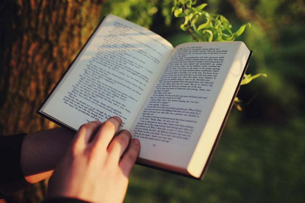 Personne debout lisant un livre ouvert à haute voix devant une fenêtre