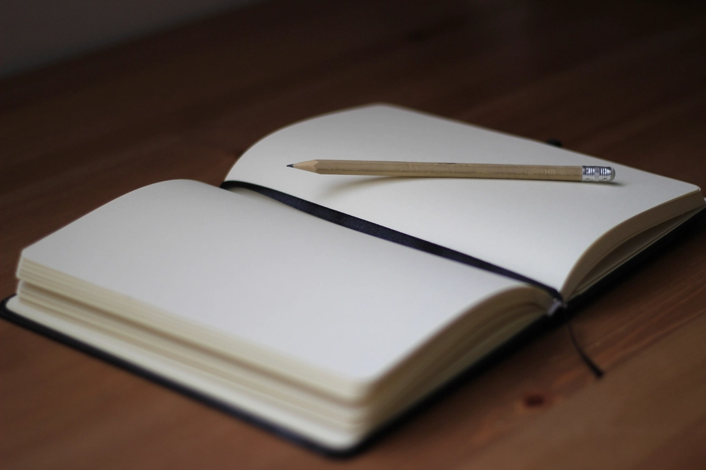 Cahier ouvert avec un crayon posé en travers, colonnes tracées à la main